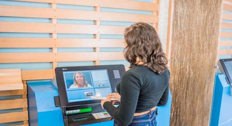 Woman standing at an Interactive Teller Machine (ITM) video chatting a financial representative